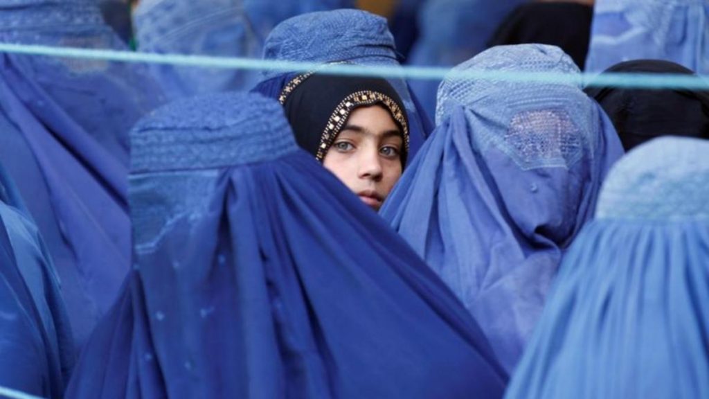 A girl looks on among Afghan women lining up to receive relief assistance, during the holy month of Ramadan in Jalalabad